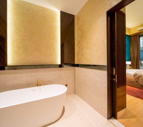 Freestanding bathtub in a backlit stone alcove with a floor-mounted brass filler, master ensuite of a Bangsar bungalow