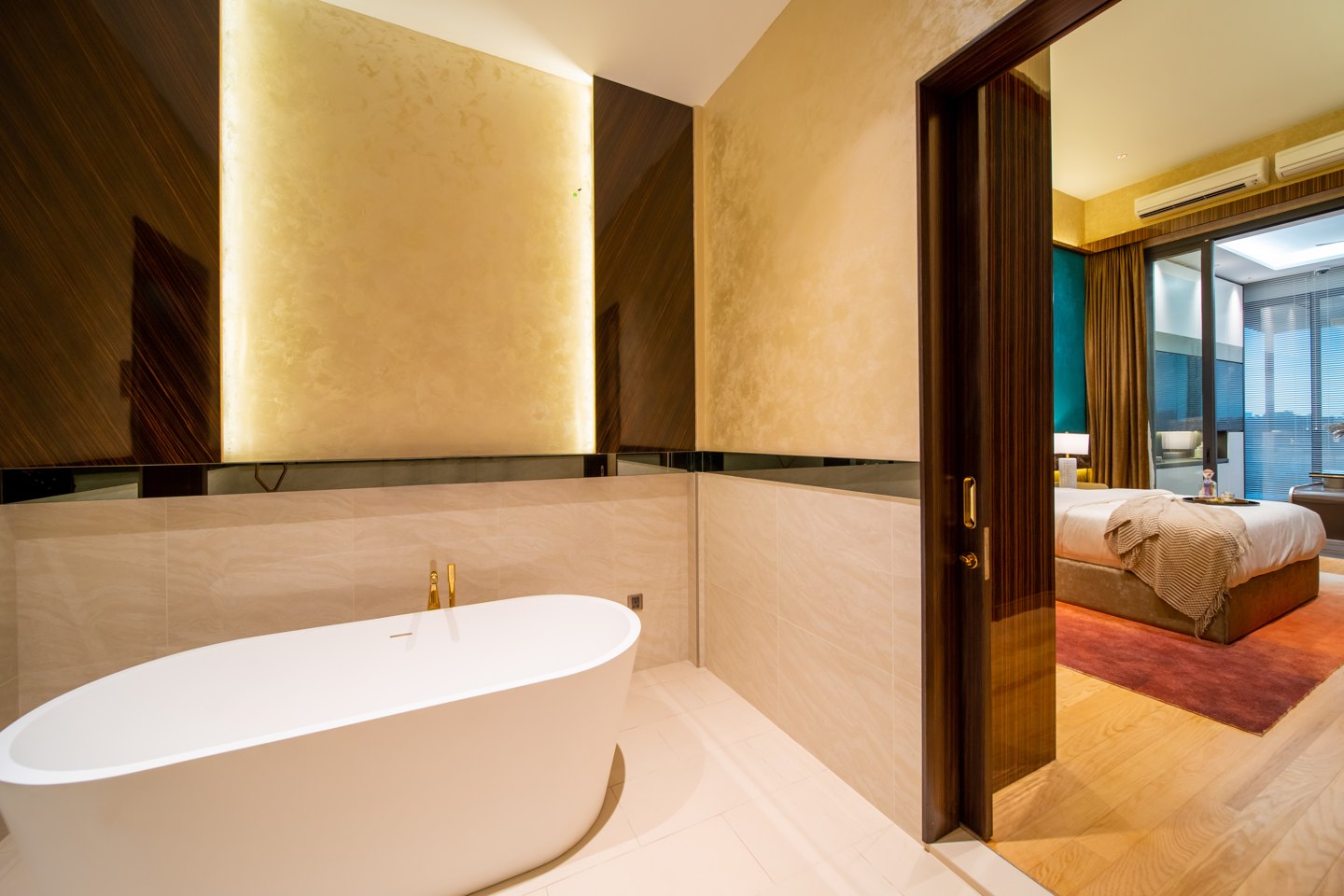 Freestanding bathtub in a backlit stone alcove with a floor-mounted brass filler, master ensuite of a Bangsar bungalow