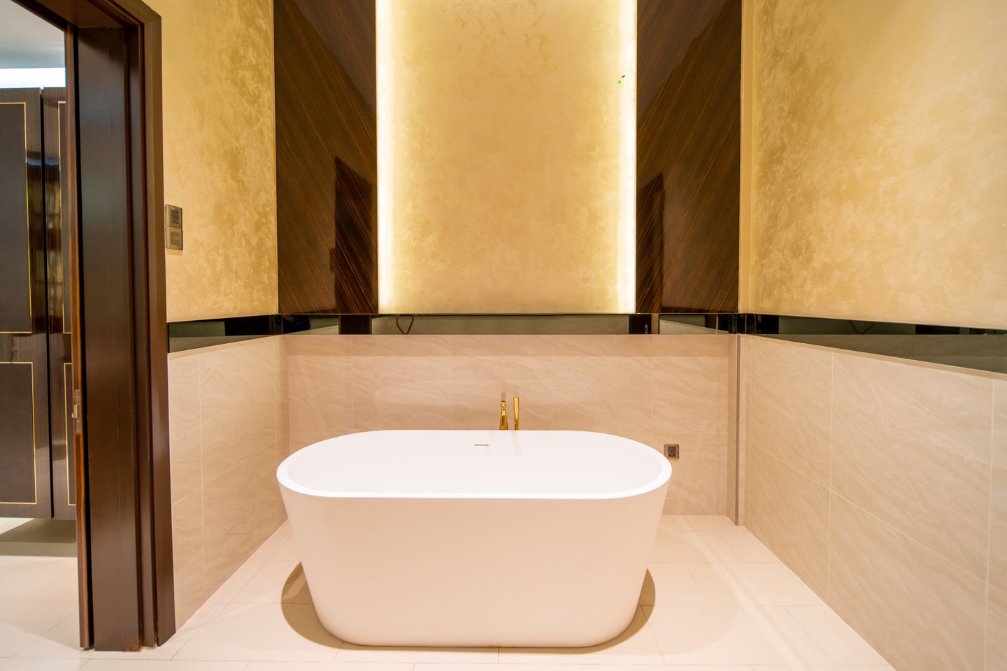Freestanding tub set in a niche of backlit textured stone with a floor-mounted brass filler, Bangsar bungalow master ensuite