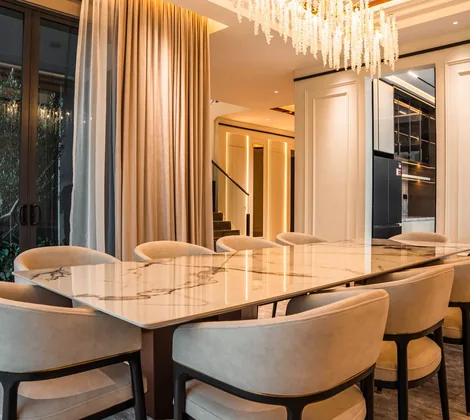 Dining room design in a Cyberjaya landed home: a long marble dining table, upholstered chairs and a crystal chandelier