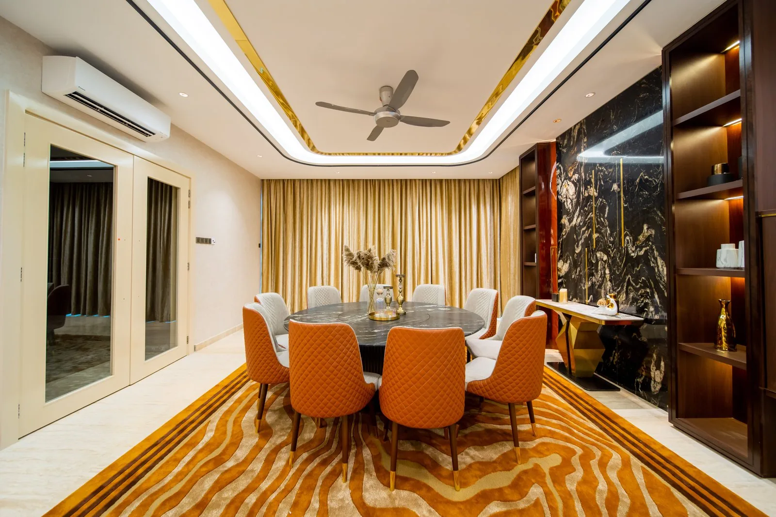 Round dining table in front of a stone wall with lit display shelving in a Bangsar bungalow