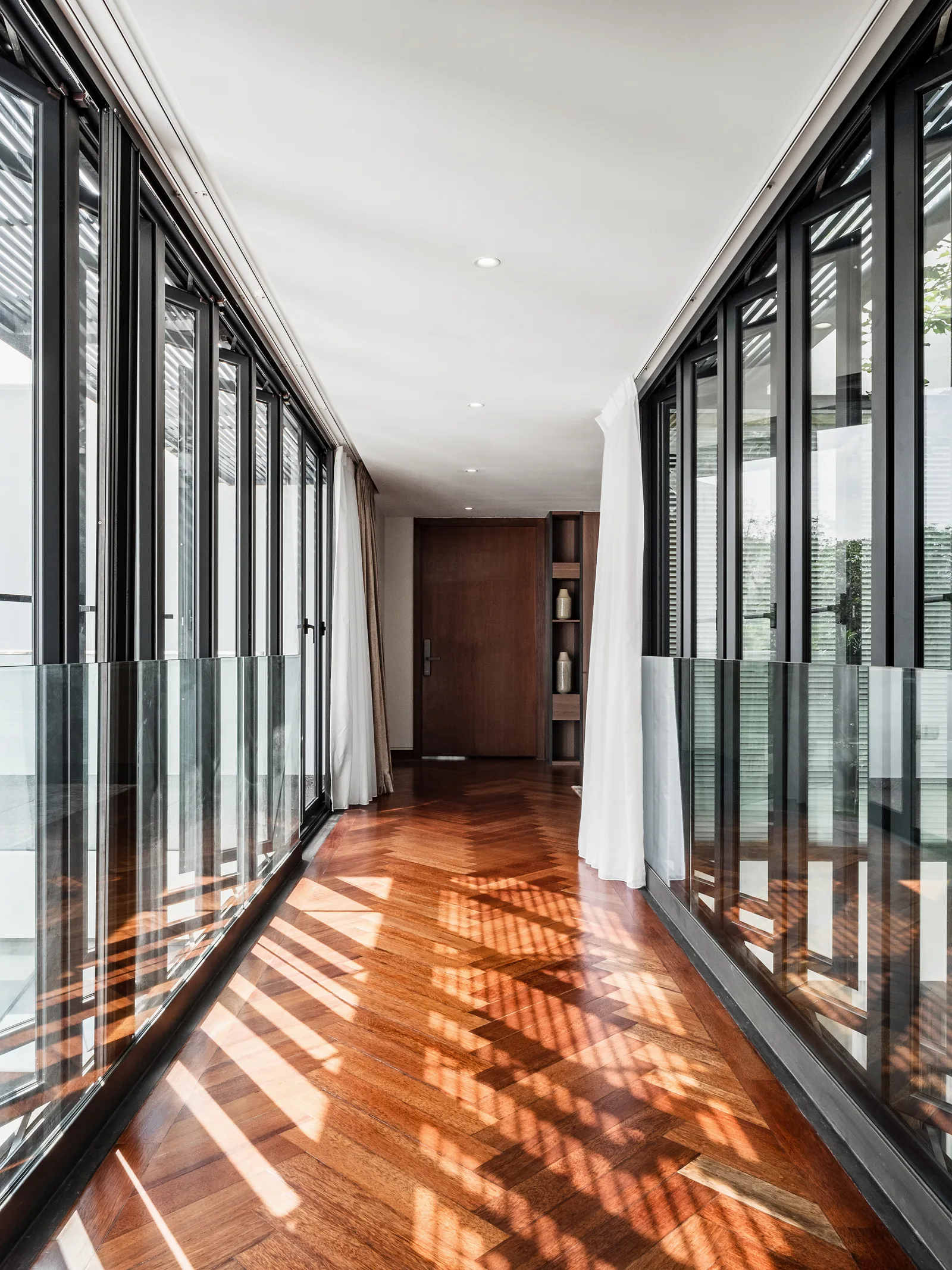 Corridor lined with full-height windows and glass balustrades, sunlight falling across a timber floor, Kelana Jaya Villa