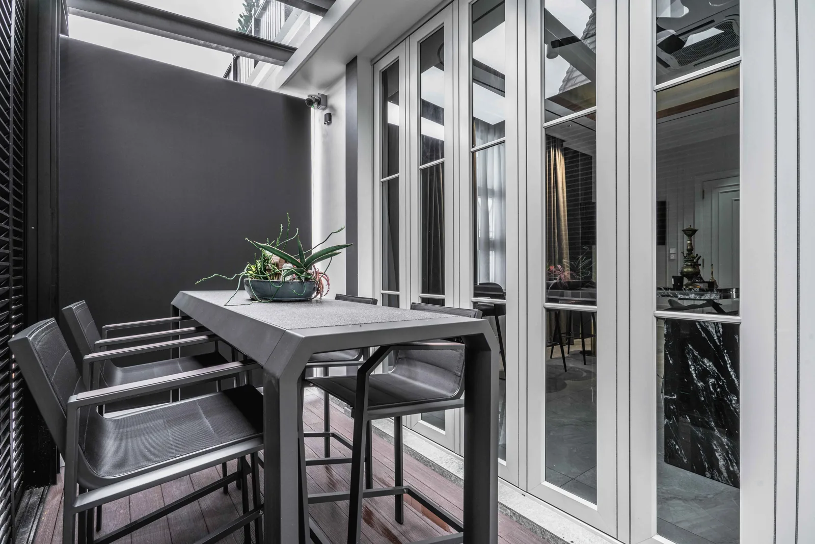Covered side terrace with a bar table, tall glass doors, a louvred screen and a glass roof, EcoSpring Villa