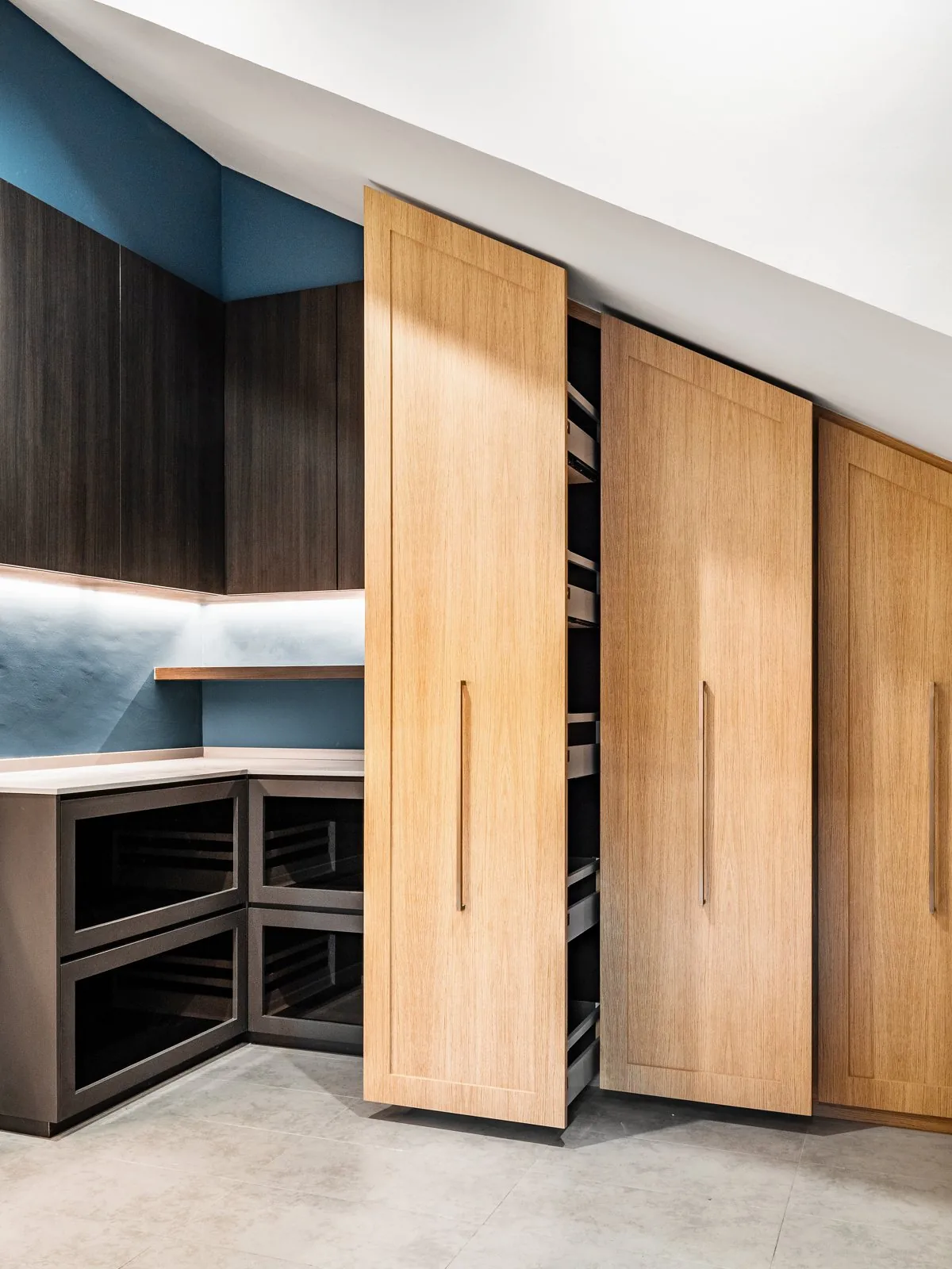 Floor-to-ceiling oak kitchen cabinets with tall pull-out units beside navy wall cabinets in a Terengganu bungalow