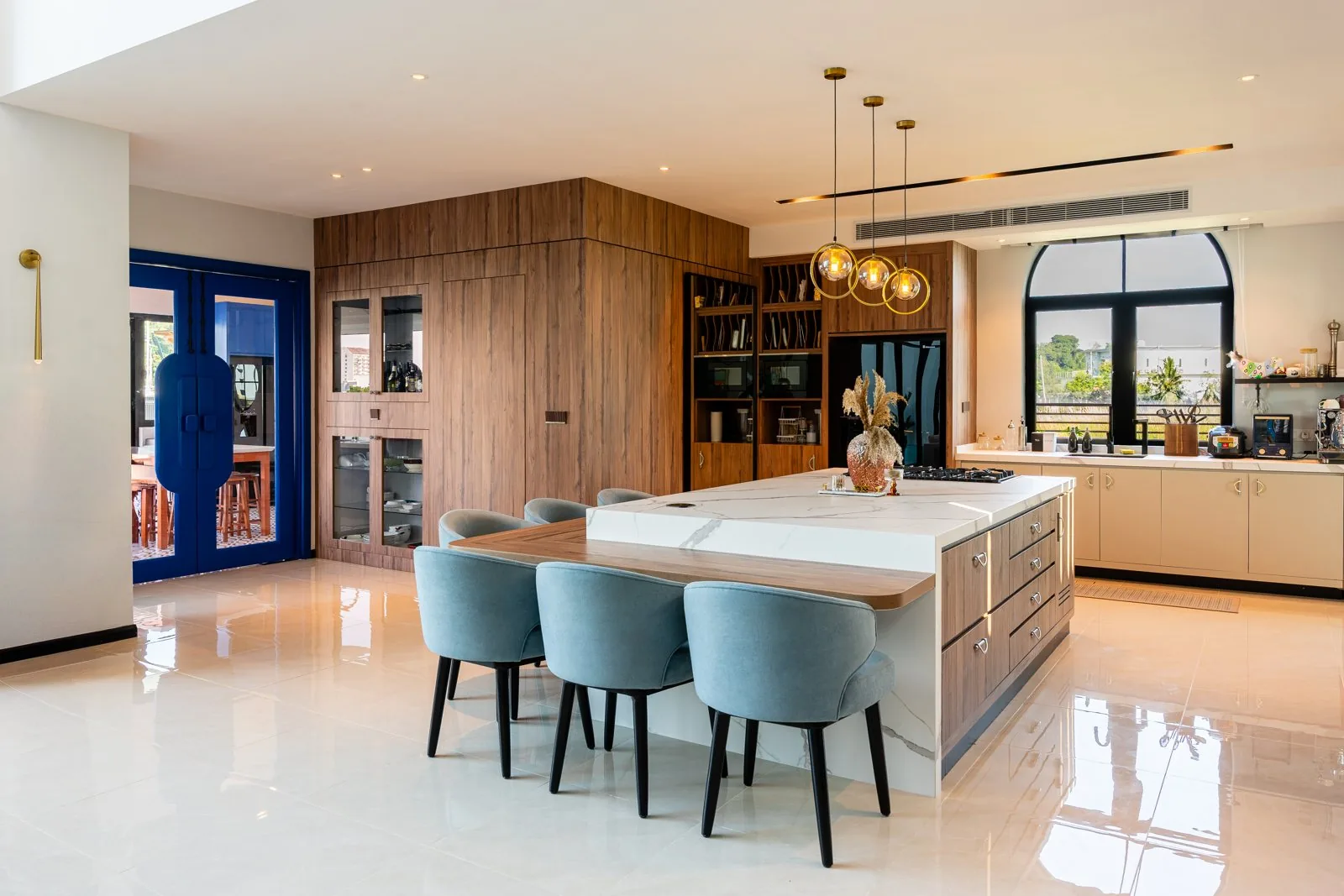 Open-plan kitchen with an island of deep drawers extending into a dining table and a tall timber cabinet wall at Quayside Villa