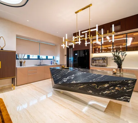 Kitchen island design with a black stone waterfall edge under a linear brass chandelier in a Bangsar bungalow, Kuala Lumpur