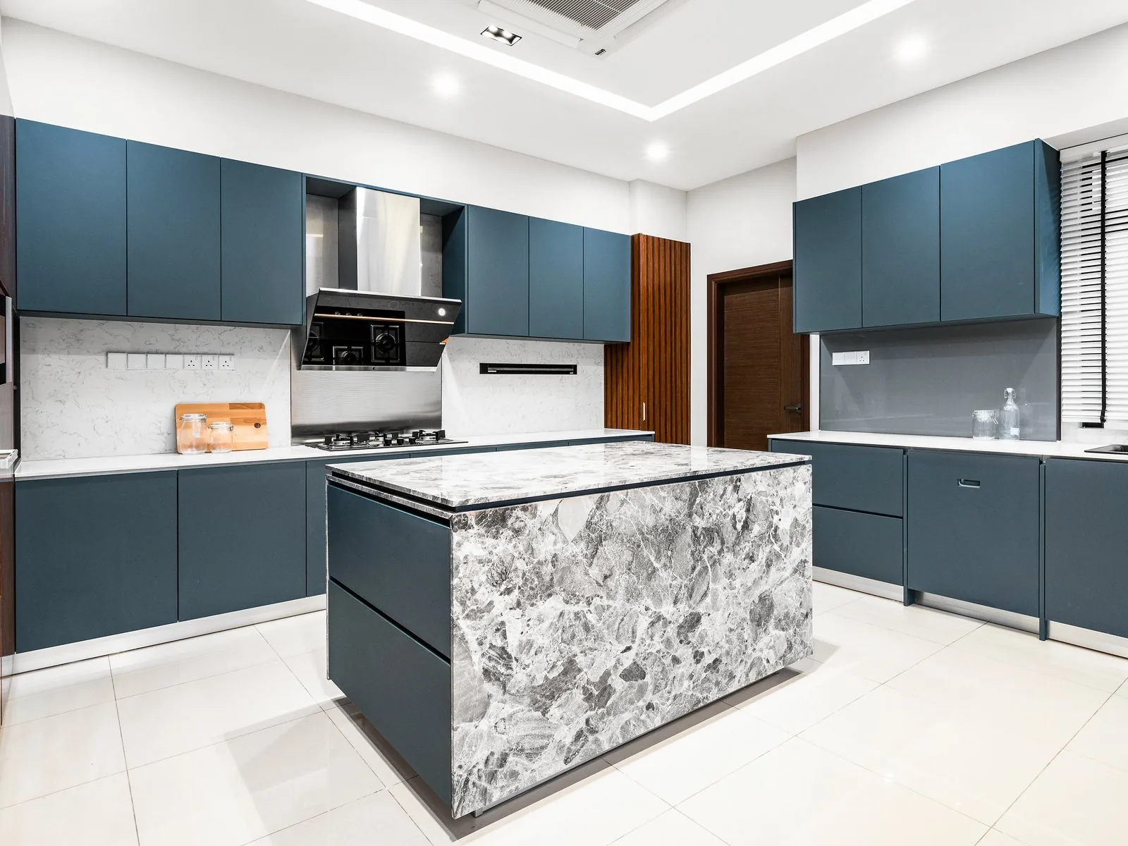 Grey patterned stone kitchen island with navy cabinets and timber panels at East Coast Villa, Terengganu