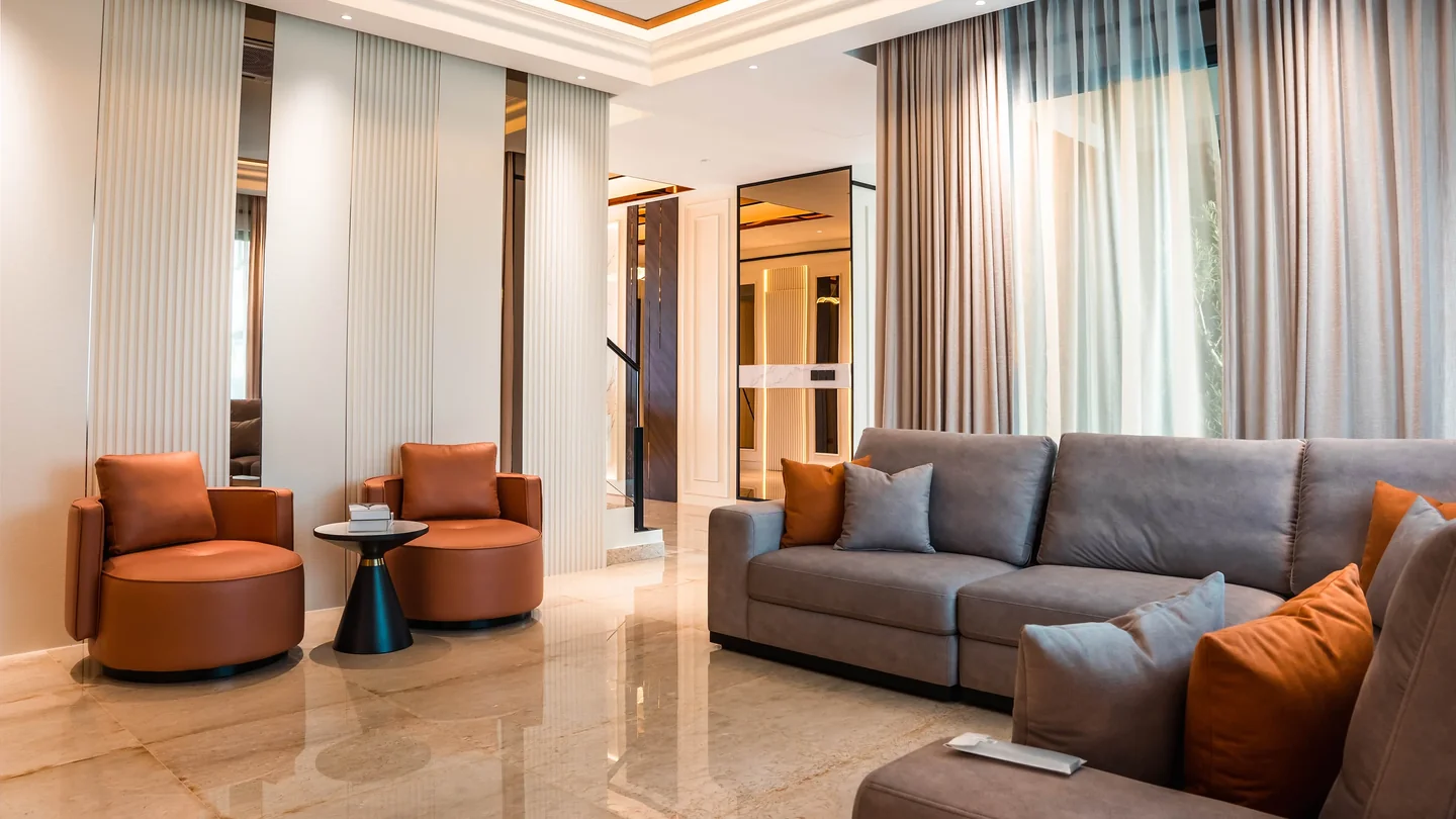 Two tan leather swivel armchairs angled toward a grey sectional for conversation, with a black side table between them, Setia Marina One