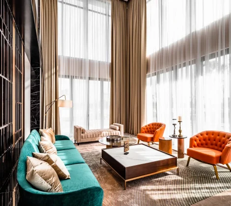 Double-height living room with a teal velvet sofa, orange armchairs and full-height windows in a Malaysian bungalow designed by Blaine Robert Design