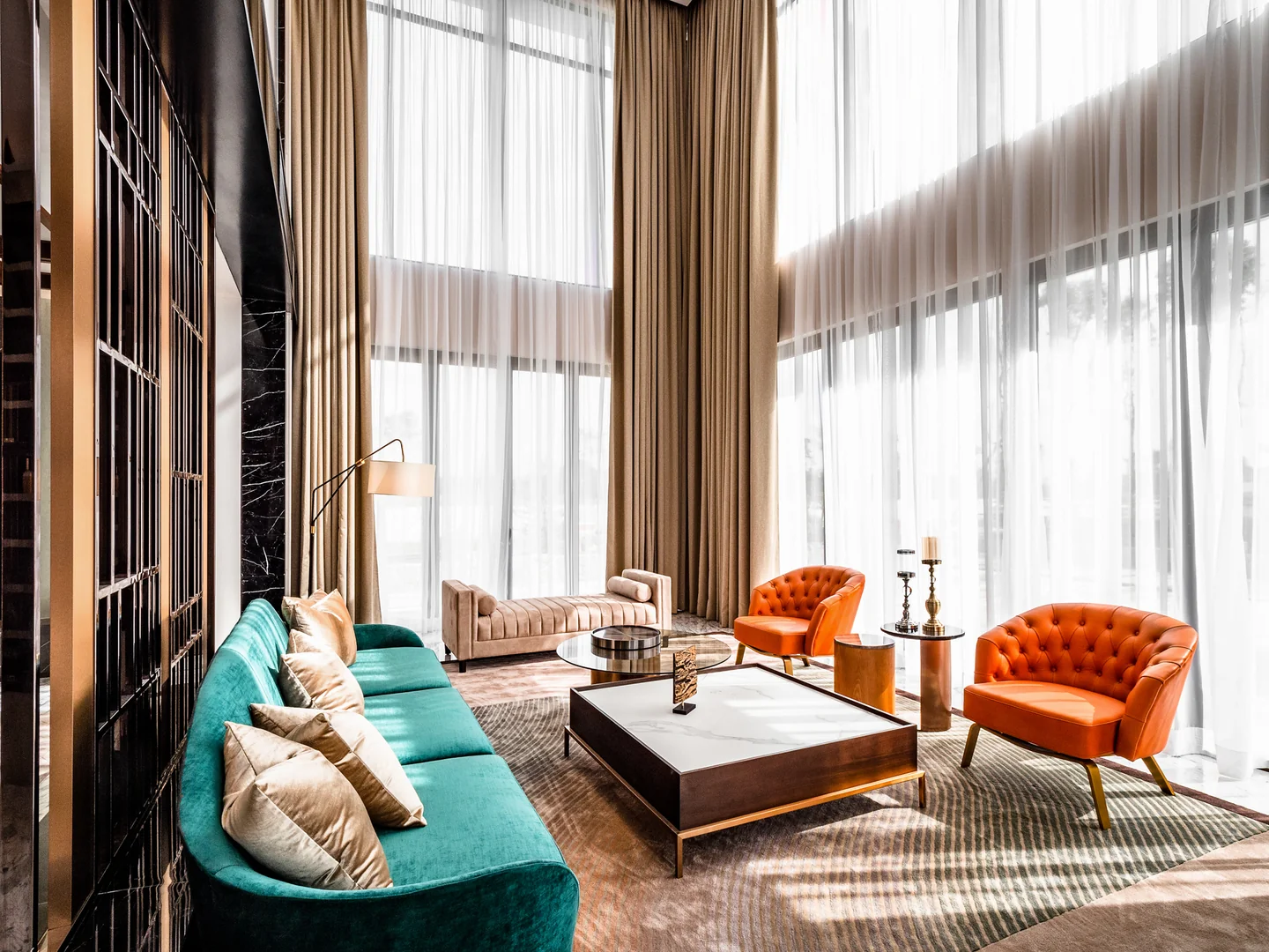Double-height living room with a teal velvet sofa, orange armchairs and full-height windows in a Malaysian bungalow designed by Blaine Robert Design