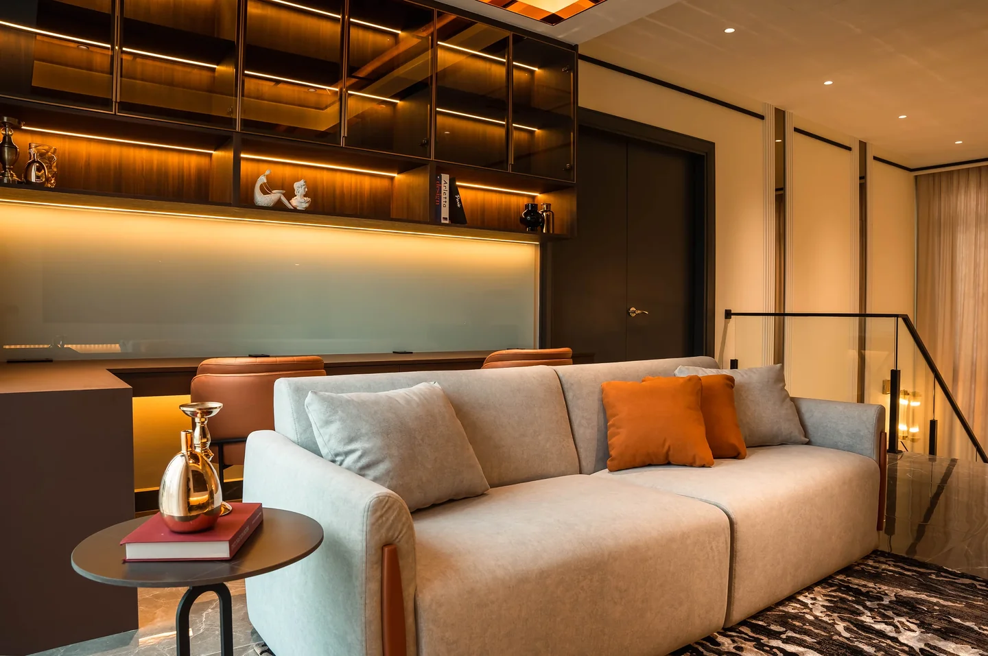 Built-in lounge shelving mixing open backlit display and closed cabinets above a beige sofa, Setia Marina One bungalow