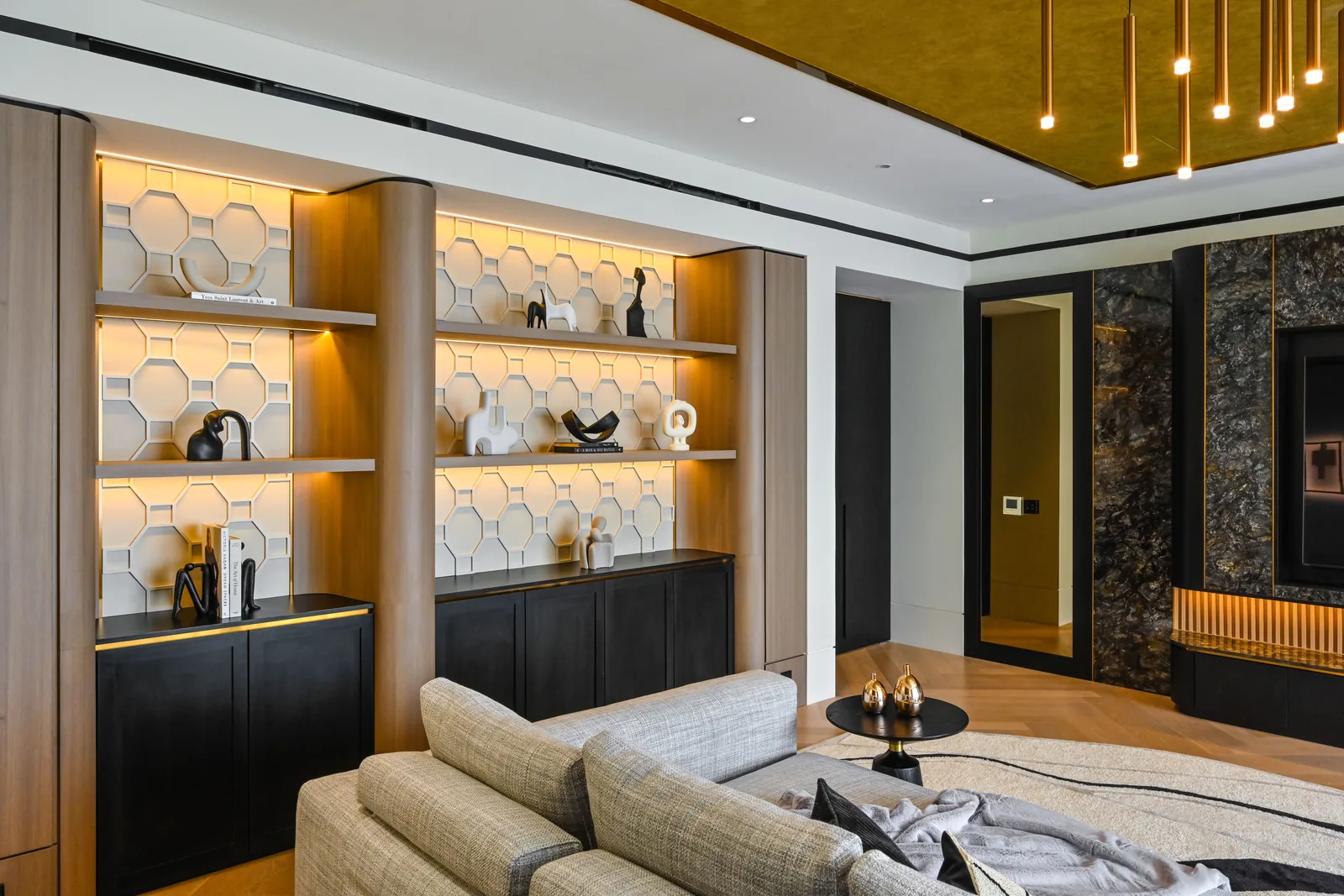 Living space with backlit shelving, a stone television wall and a warm palette at Aira Residence, Damansara Heights