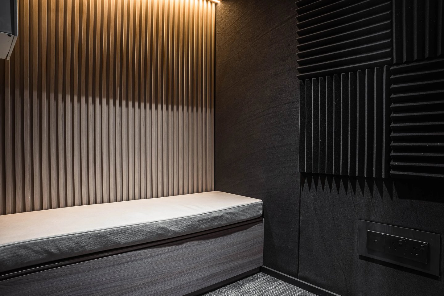Built-in window bench against fluted timber panelling and a dark acoustic panel wall at Setia Marina One