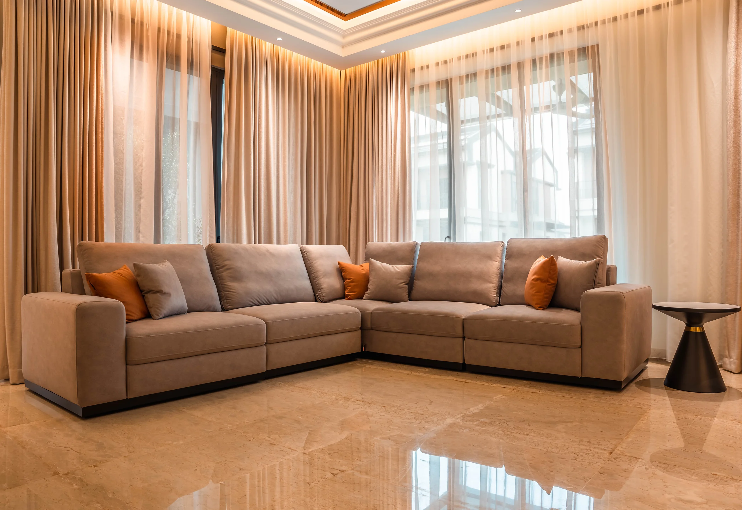 L-shaped sectional sofa anchoring the corner of a living hall at Setia Marina One, a landed home in Cyberjaya, with layered sheer curtains and cove lighting.