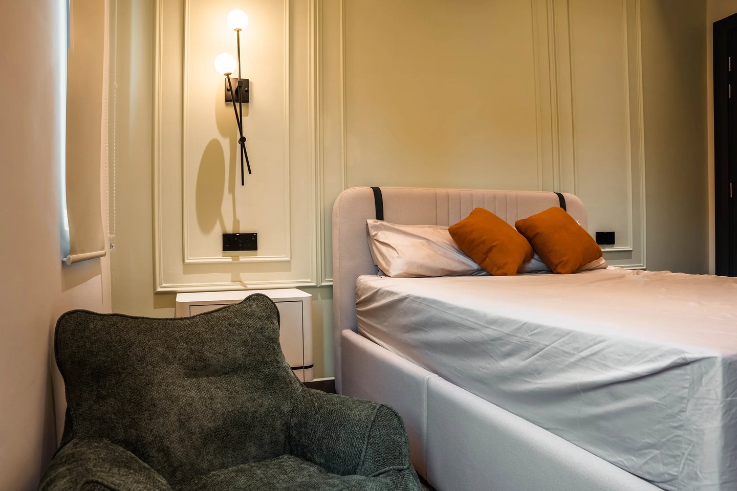 Bedroom with classical wall panelling in sage, brass wall sconce and a textured accent armchair at Setia Marina One