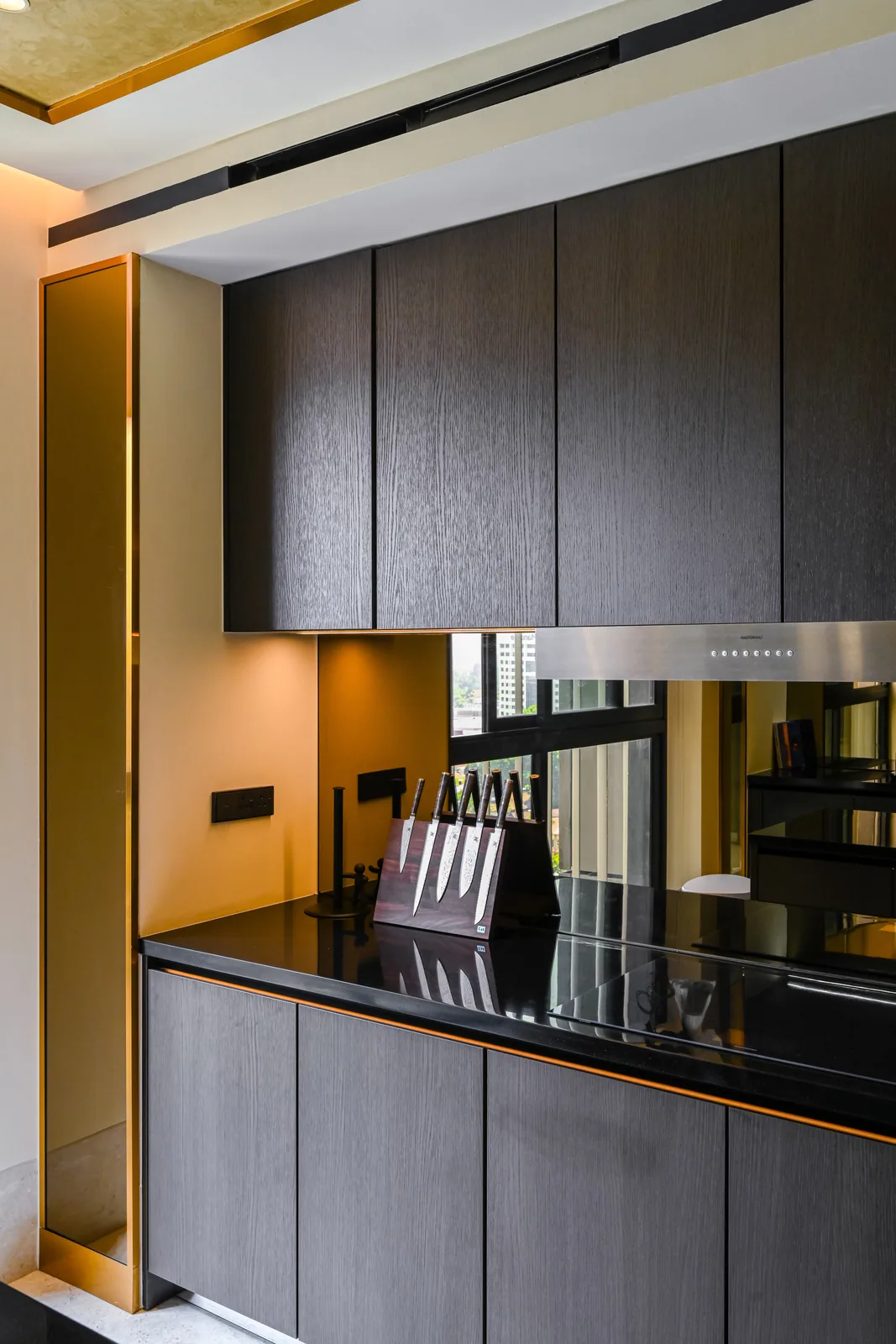 Compact kitchen with dark timber cabinets, a black stone worktop and a mirrored backsplash at Aira Residence, Damansara Heights