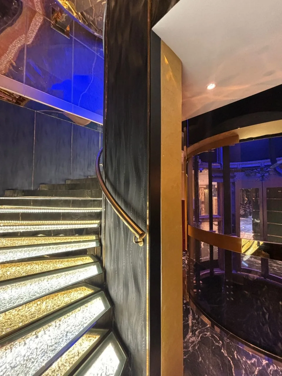 Curved staircase with lit treads beside a cylindrical aquarium at The Peak, Ampang